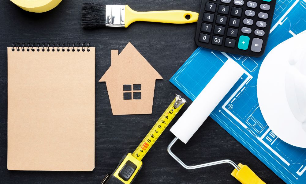 Strumenti per ristrutturazione e miglioramento dell'efficienza energetica, come metro e pennello da pittura, simbolizzano lavori di rinnovamento e manutenzione ordinaria degli edifici.